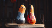 Two yellow gourds painted to look like a frowning man with black hair wearing a blue top and a smiling woman with long black hair and a red and white dress sit on a ledge.